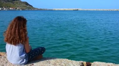 Gökceada Kuzulimani 'de sırtı deniz kenarında oturan bir kız denize çakıl taşları atıyor. Imbros Adası Gkeada, Türkiye