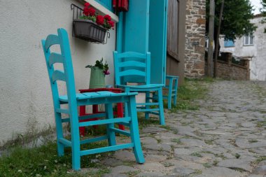 Gökçeada 'daki eski bir Yunan köyü olan Gliki' deki ev duvarına karşı mavi sandalyeler ve ahşap kırmızı tabure. Çanakkale, Türkiye. 