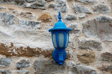 Eski bir Akdeniz tarzı taş binanın ön cephesinde eski bir mavi sokak feneri. Romantik tarihi sokak lambası desenli arka plan. Kopya alanı ile Ege adası kavramı