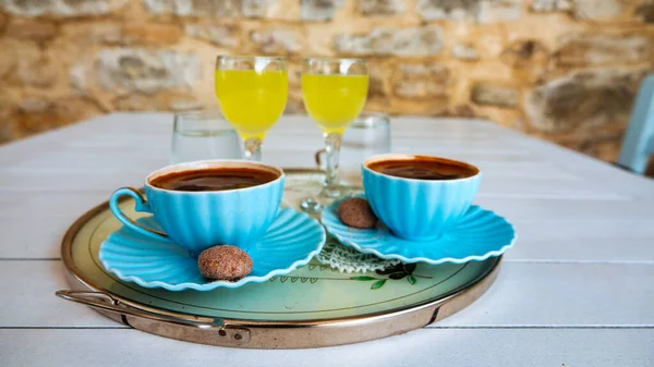 小さなクッキーとレモンリキュールまたは白い木製のテーブルの上にトレイ上のライモンチェッロを提供トルココーヒーの2つのカップ — ストック写真