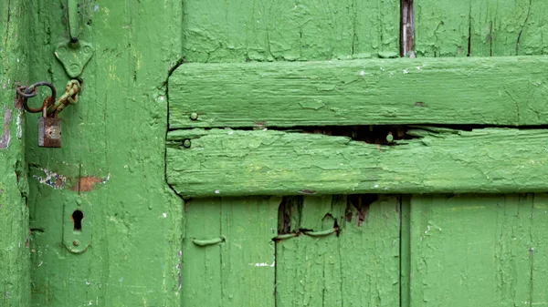 An old wooden door painted green with a rusty padlock on it. copy space vintage wallpaper
