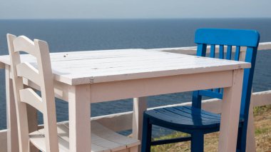 Tepedeki deniz kenarında bir Akdeniz restoranında beyaz mavi masa ve sandalyeler.