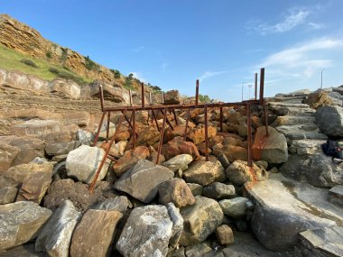 Deniz kenarındaki kayalıklarda terk edilmiş paslı bir rıhtım platformu. Paslı çelik kirişler, eski iskele kalıntıları.