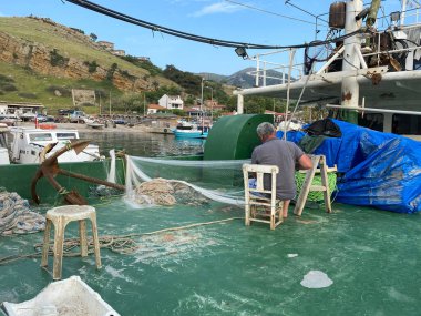 Gökçeada, Canakkale, Türkiye, 28 Mayıs 2023: Gemi güvertesinde geleneksel balıkçı ağları ören bilinmeyen bir balıkçı 