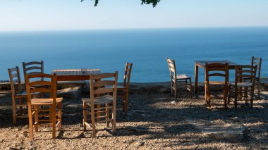 Gökçeada (Imbros) kıyı şeridi ve ahşap sandalyeli ve masalı şirin bir köy çay bahçesi manzarası. Tepeky köyü, Naralt-Pinarbasi bölgesi, Ege Türkiye