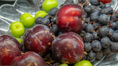 Yeşil ve kırmızı eriklerin yakın görüntüsü, cam bir tabakta siyah üzümler