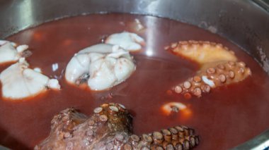 Haşlanmış ahtapot çeşitli otlar ve defne yapraklarıyla marine edilmiş büyük bir tencerede.