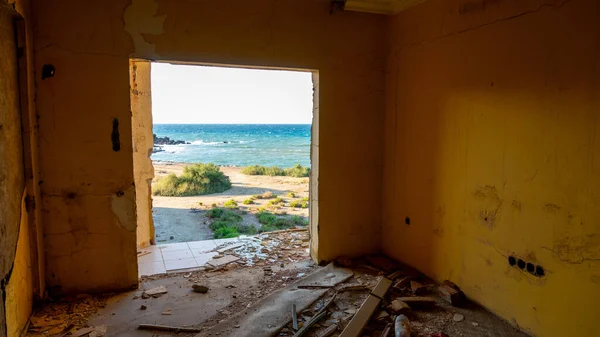 破壊された窓を通る海岸線の景色は 廃墟となった古いホテルの建物の部屋です 壊れた窓から海を眺める — ストック写真