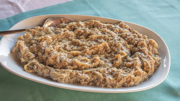 Geleneksel lezzetli Türk yemekleri; restoran masasında servis edilen büyük porselen tabakta sarımsaklı yoğurtla kızartılmış patlıcan. Tabakta kızarmış patlıcan taratörü var.