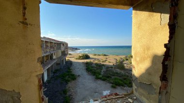 Terk edilmiş ve yıkılmış eski bir otel binasının kırık penceresinden kıyı şeridi manzarası. Kırık bir pencereden denize bak.  