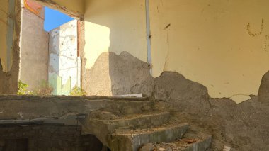 Terk edilmiş ve yıkılmış eski bir otel binasının çatısına çıkan merdivenler ve etrafa saçılmış inşaat enkazı.