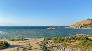 Rüzgarlı bir günde Kalekoy limanı, arka plandaki yüksek dağda demirli tekneler ve Kalekoy kalesi. Gökçeada, Çanakkale, Türkiye