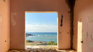 Terk edilmiş ve yıkılmış eski bir otel binasının kırık penceresinden kıyı şeridi manzarası. Kırık bir pencereden denize bak.  