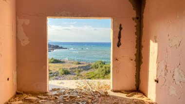 Terk edilmiş ve yıkılmış eski bir otel binasının kırık penceresinden kıyı şeridi manzarası. Kırık bir pencereden denize bak.  