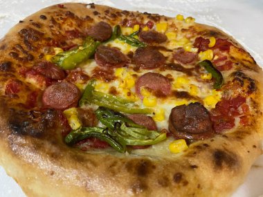 Mısır, biber ve sosisli geleneksel İtalyan pizzası mermer tezgahta etrafa un saçılmış. Seçici odak, kapat.