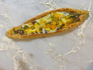 Mermer tezgahta yumurta, biber ve kıymalı ev yapımı Türk pidası pizzası ve etrafa un saçılmış. Geleneksel Türk mutfağı. Kapat, seçici odak