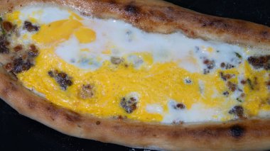 Türk pidesi ya da Türk pizzası düz ekmeği ve her iki ucuna da doğranmış et ve sebze, peynir ve yumurta veya farklı kombinasyonlarla doldurulmuş. Görüntüyü kapat, siyah tabakta servis yap