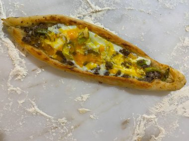 Mermer tezgahta yumurta, biber ve kıymalı ev yapımı Türk pidası pizzası ve etrafa un saçılmış. Geleneksel Türk mutfağı. Kapat, seçici odak