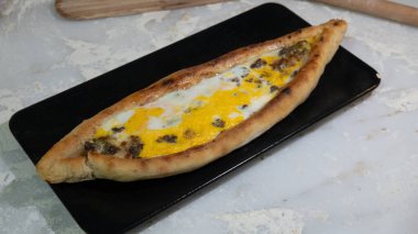 Türk pidesi ya da Türk pizzası düz ekmeği ve her iki ucuna da doğranmış et ve sebze, peynir ve yumurta veya farklı kombinasyonlarla doldurulmuş. Siyah tabakta, mermer tezgahın üzerinde un etrafa saçılmış..