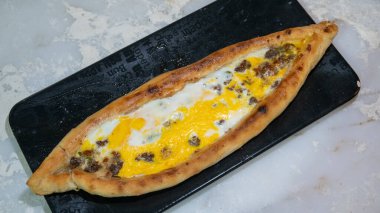 Türk pidesi ya da Türk pizzası düz ekmeği ve her iki ucuna da doğranmış et ve sebze, peynir ve yumurta veya farklı kombinasyonlarla doldurulmuş. Siyah tabakta, mermer tezgahın üzerinde un etrafa saçılmış..