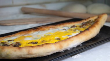 Türk pidesi ya da Türk pizzası düz ekmeği ve her iki ucuna da doğranmış et ve sebze, peynir ve yumurta veya farklı kombinasyonlarla doldurulmuş. Siyah tabakta, mermer tezgahın üzerinde un etrafa saçılmış..