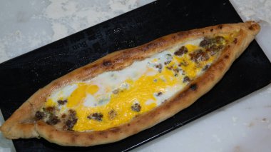 Türk pidesi ya da Türk pizzası düz ekmeği ve her iki ucuna da doğranmış et ve sebze, peynir ve yumurta veya farklı kombinasyonlarla doldurulmuş. Siyah tabakta, mermer tezgahın üzerinde un etrafa saçılmış..