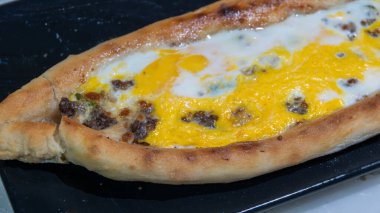 Türk pidesi ya da Türk pizzası düz ekmeği ve her iki ucuna da doğranmış et ve sebze, peynir ve yumurta veya farklı kombinasyonlarla doldurulmuş. Görüntüyü kapat, siyah tabakta servis yap