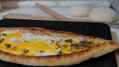 Türk pidesi ya da Türk pizzası düz ekmeği ve her iki ucuna da doğranmış et ve sebze, peynir ve yumurta veya farklı kombinasyonlarla doldurulmuş. Siyah tabakta, mermer tezgahın üzerinde un etrafa saçılmış..