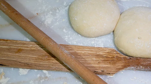 Preparation of raw dough balls with a rolling pins  for cooking pastries on a on the marble counter with flour scattered around.  Traditional Turkish cuisine. close up, selective focus