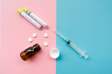 Haplı boş cam şişe, iki pozitif koronavirüs testi ve şırınga. pembe ve turkuaz minimalist arkaplan kavramı