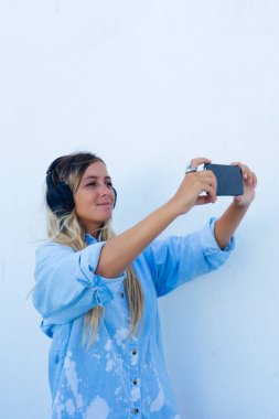 Kadın telefonda müzik dinlerken selfie çekiyor. Beyaz arkaplan