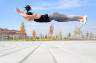 Spor yapan kadın sokakta yerde egzersiz yapıyor.