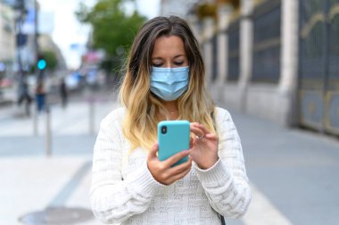 Maskeli kadın şehir trafiği geçmişi olan bir telefon kullanıyor.