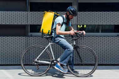 Bisikletle yiyecek getiren sakallı genç kurye akıllı bir telefonla siparişi kontrol ediyor. Teslimat hizmeti kavramı.