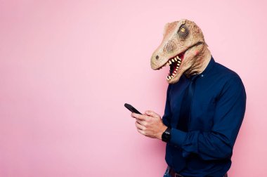 Dinozor maskeli adam akıllı telefon kullanıyor. Pembe arka plan..