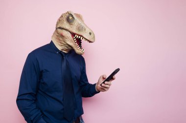 Dinozor maskeli adam akıllı telefon kullanıyor. Pembe arka plan.
