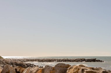Cape Town Şaraphaneleri yakınlarında sakin bir günbatımı sahnesi, sahil şeridinin huzurlu güzelliğini yakalıyor. Resim, yumuşak, pastel bir gökyüzünün altında yumuşak dalgaların taşlara çarptığı kayalık bir sahili gösteriyor. Sakinlik ve rahatlama uyandırmak için idealdir.