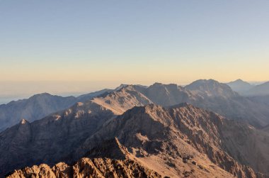 Gün batımının sıcak, altın ışığında yıkanan engebeli dağ tepelerinin nefes kesici manzarası. Görüntü Imlil ve Toubkal Dağı 'ndaki yürüyüşün özünü yakalıyor ve bir macera ve sükunet hissi uyandırıyor. Seyahat, doğa ve açık hava yaşamı için ideal.
