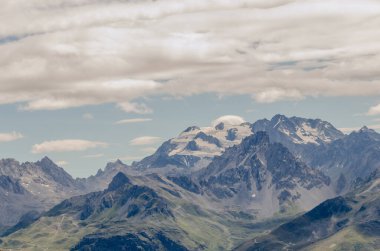 Fransız Alpleri 'nin, parçalı bulutlu bir gökyüzünün altında engebeli, karla kaplı tepelerini gösteren nefes kesici bir manzarası. Görüntü, dağların dingin güzelliğini ve ihtişamını yakalıyor. Macera ve sükunet hissi uyandırmak için ideal. Yolculuk için mükemmel, Nat.