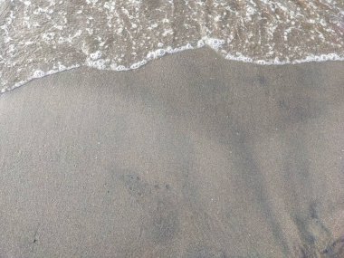 Deniz suyundan sonra kalan köpük, temiz kumla dolu bir kumsalda denize geri döner..