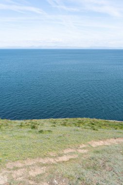 BlueBell çiçekleriyle yeşil çimlerin üzerinden ufka uzanan mavi bir okyanusa uzanan bir patika kesiliyor..