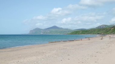 İngiltere, Morfa Nefyn 'deki kumlu kumlu sahile. Groyne, okyanus dalgaları ve ufuktaki dağlara doğru uzanan bir körfez manzarası..