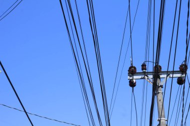 Parlak mavi gökyüzü arka planında elektrik kabloları olan elektrik direği..