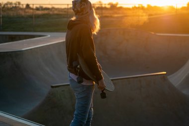 Kaykaycı kadın kaykaycı gün batımında kaykay parkındaki yarım boru rampasında ışığa karşı.