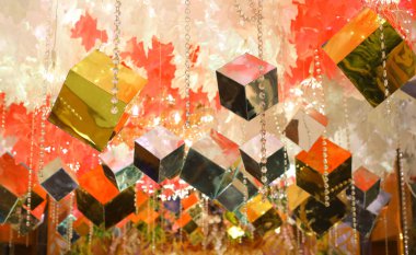 Altından, gümüşten ve yanardöner renkte parlak yansıtıcı küplerin göz kamaştırıcı görüntüsü, zarif beyaz ve turuncu çiçeklerle süslenmiş, canlı ve zarif bir ortam yaratıyor..