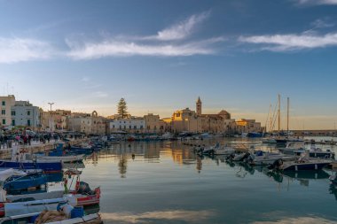 Gün batımında Trani limanının panoramik manzarasında balıkçı tekneleri, balıkçı tekneleri ve San Nicola Pellegrino Bazilikası var. Puglia, İtalya.
