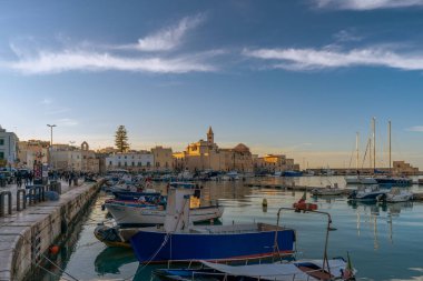 Gün batımında Trani limanının panoramik manzarasında balıkçı tekneleri, balıkçı tekneleri ve San Nicola Pellegrino Bazilikası var. Puglia, İtalya.