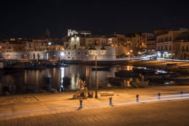 Bisceglie 'nin antik limanında gece ışıkları deniz ve aydınlatılmış tarihi köy Puglia' yı yansıtıyor (Apulia), İtalya