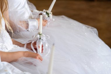 İlk Komünyon. Kızlar ellerinde çiçeklerle süslenmiş sönmüş bir mum tutarak oturuyorlar. Harika ya da güzel tatil elbiseleri