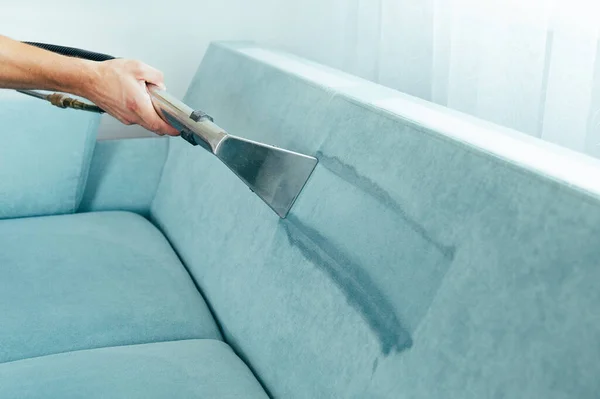 清洁的概念 男人打扫房间里的青色沙发 病毒预防在里面消毒 深层家具清洗的过程 专业的化学清洗 小企业贷款 图库照片